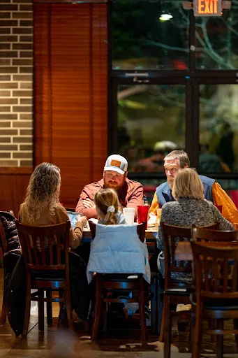 A family with a child sharing dinner at a wooden table inside Casa Pirul's dining room, with drinks on the table and brick walls behind them
