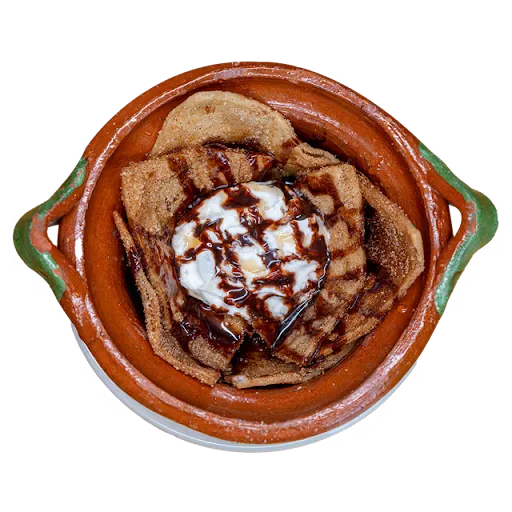 Cinnamon-sugar sopapillas in a green-handled clay dish, topped with ice cream and chocolate drizzle, seen from above