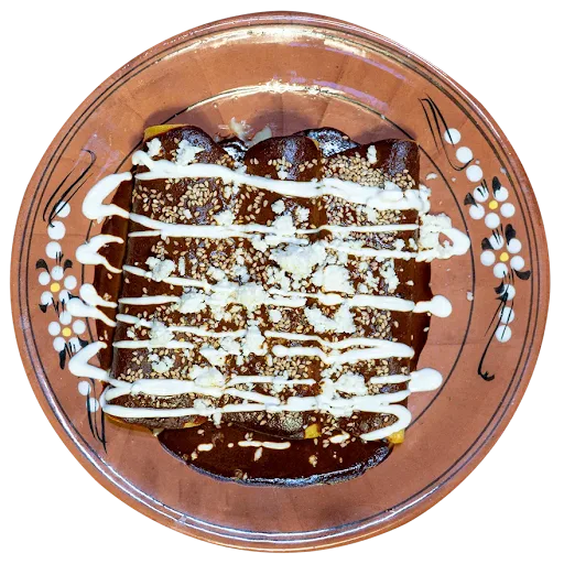 Enchiladas con mole drizzled with crema and topped with sesame seeds on a hand-painted clay plate